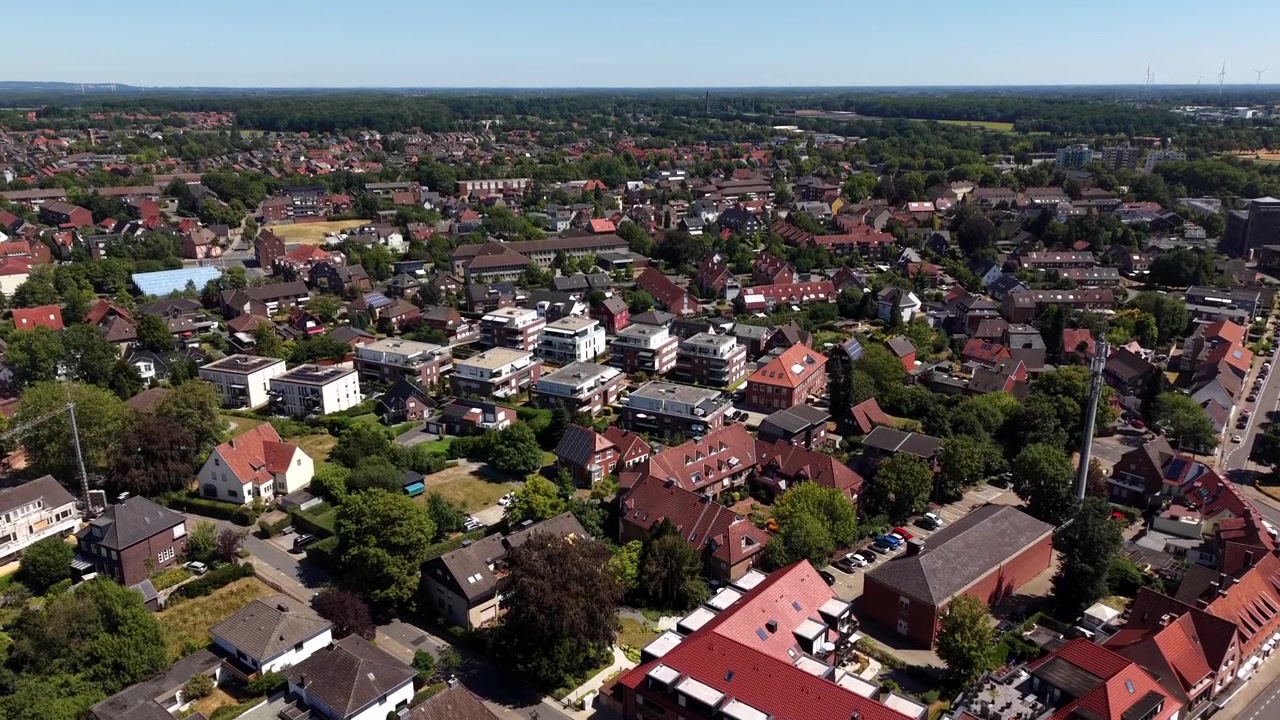 Blandede boligtak spredt over et lite tysk sentrum, røde teglsteinshus og hvite leilighetsbygg ligger blant trekantede gater under rolig sommersol. Luftfoto med drone som stiger opp.