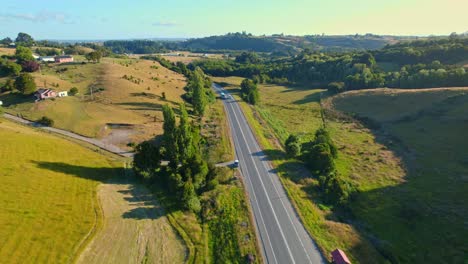 Eine-Landstraße-Auf-Der-Insel-Chiloé,-Sonniger-Tag-Mit-Vereinzelten-Wolken,-Grüne-Landschaft,-Luftaufnahme