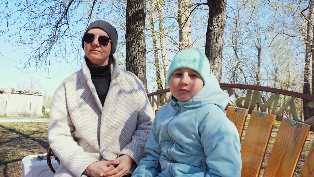Matka i córka siedzące na ławce w słonecznym parku