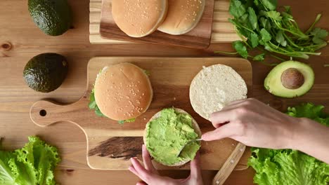 crop woman spreading avocado on hamburger bun