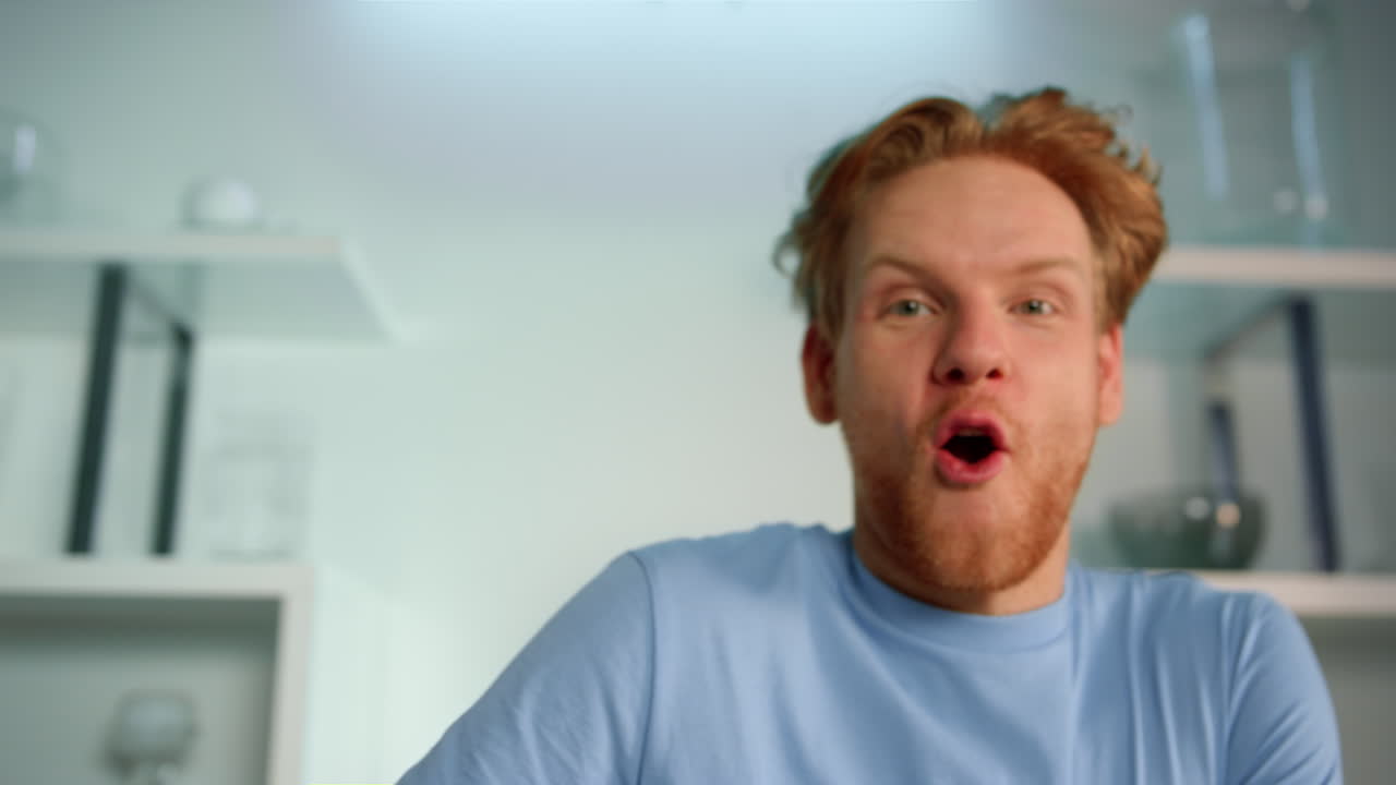 흥분 된 남자가 블로그 비디오를 클로즈업으로 녹화하고 있습니다. 미소 짓는 홍색 남자가 카메라에 손을 흔들고 있습니다.