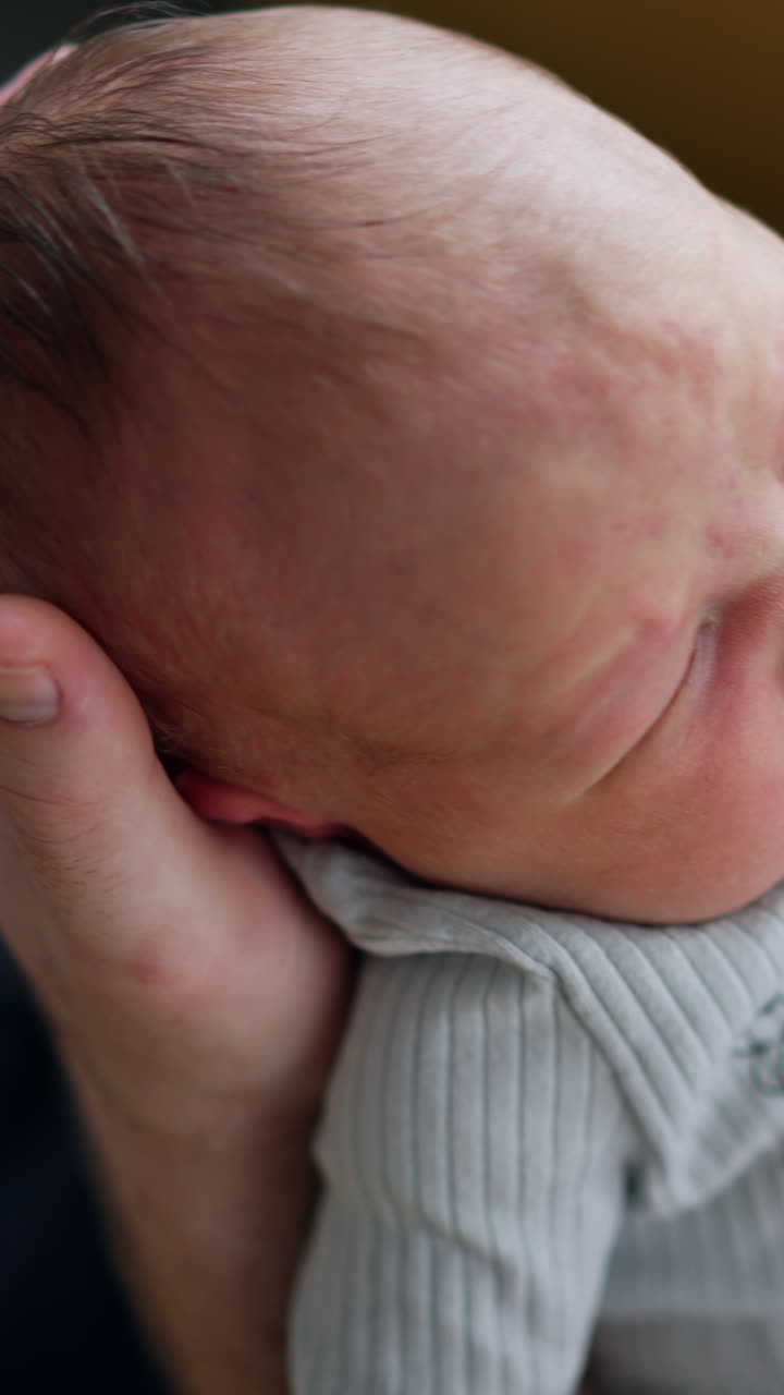 Baby boy cries lying on the big hand of his dad. Newborn makes a wry face and then calms down. Close up. Vertical video