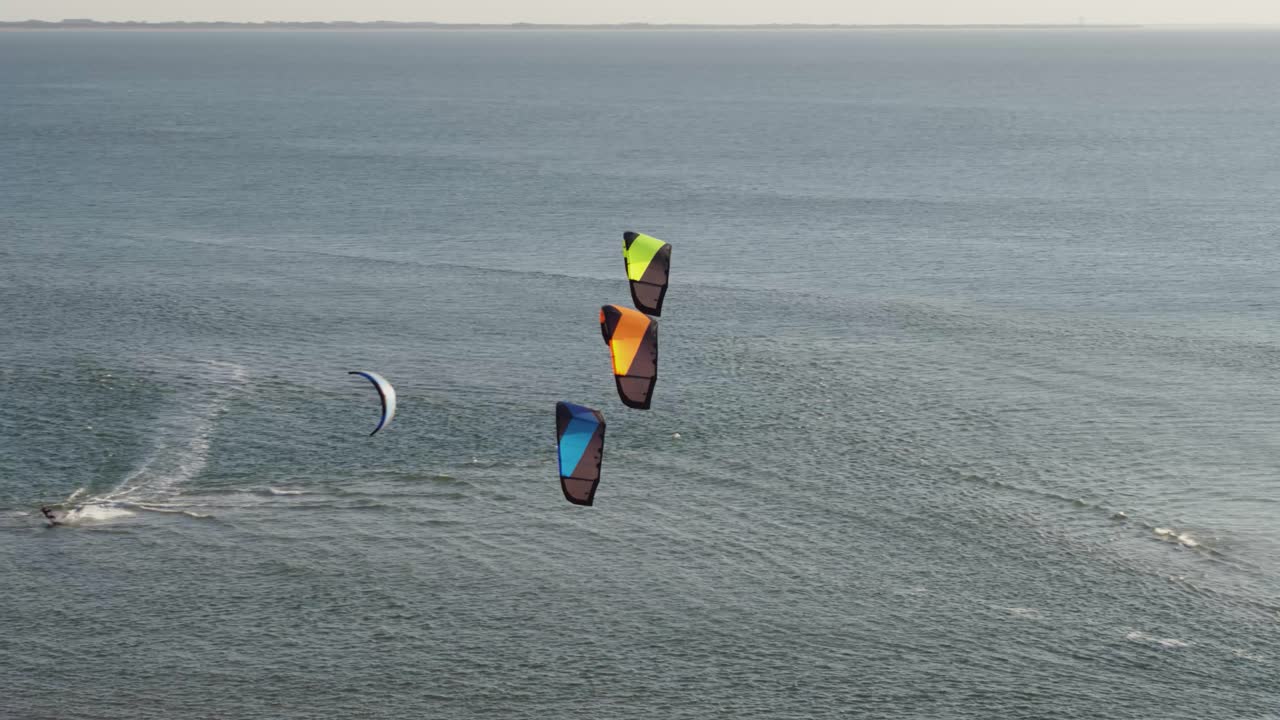 tres cometas multicolores se ciernen frente a un kitesurfer montando dutch bay