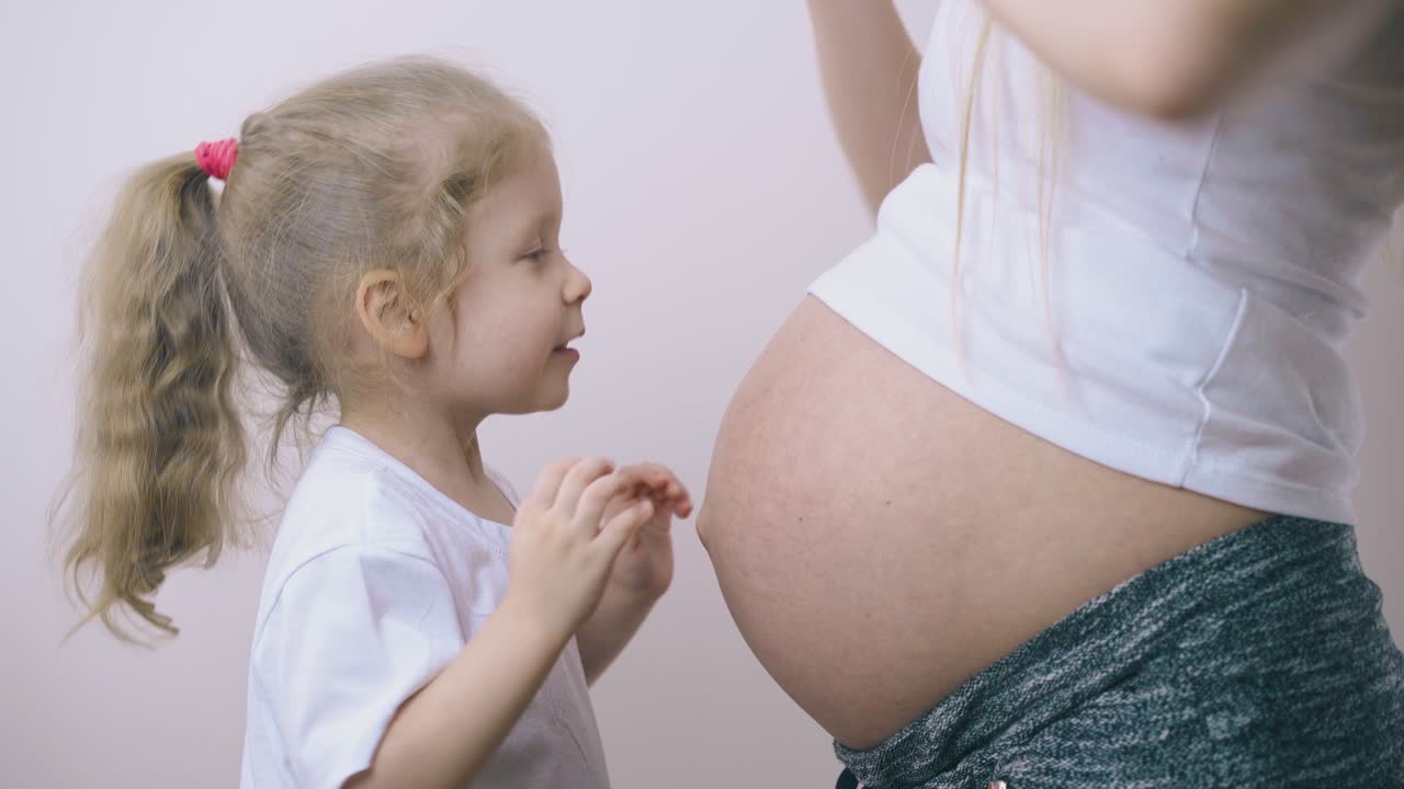 la niña juega con el estómago de la madre embarazada en casa
