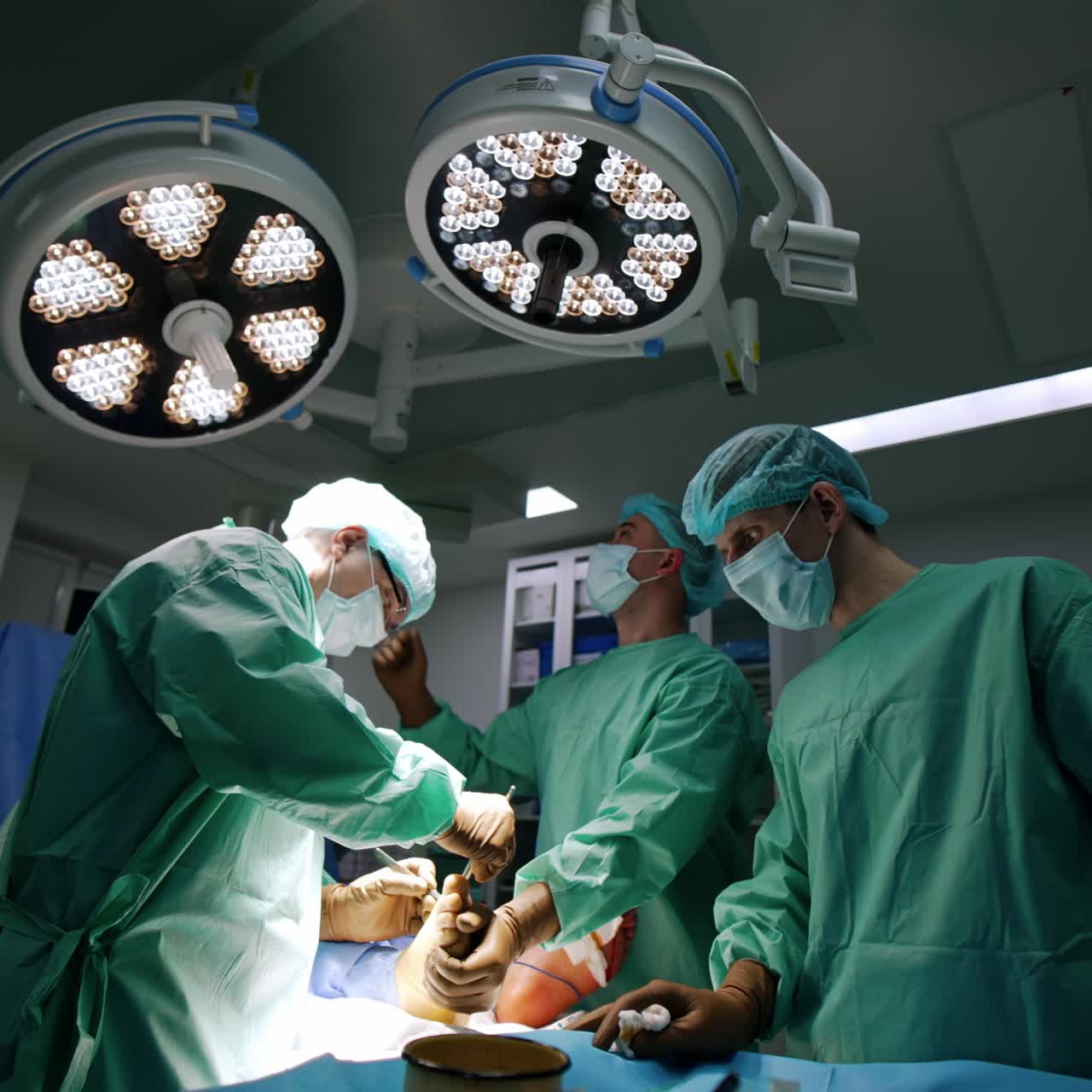 Equipo quirúrgico operando un traumatismo en el pie. Un médico acerca la lámpara redonda para iluminar la zona de la operación. Vista desde un ángulo bajo.