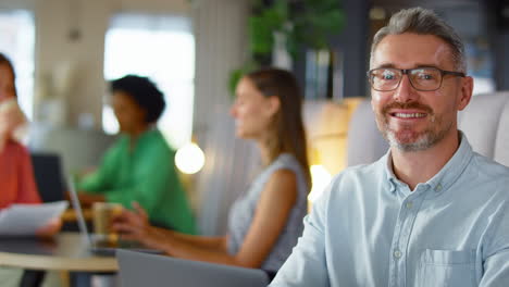 Portrait-Of-Mature-Businessman-Working-On-Laptop-In-Informal-Seating-Area-Of-Modern-Office