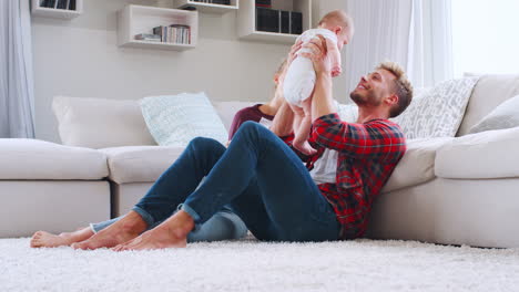 Young-white-couple-sit-lifting-baby-at-home,-side-view
