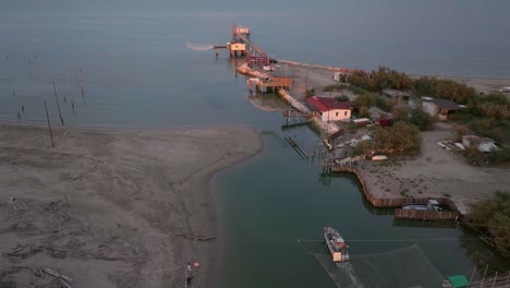 Luftaufnahme-Von-Fischerhütten-Am-Ufer-Der-Mündung-Bei-Sonnenuntergang,-Italienische-Fischermaschine,-Genannt-&quot;Trabucco&quot;,-Lido-Di-Dante,-Ravenna-In-Der-Nähe-Des-Comacchio-Tals