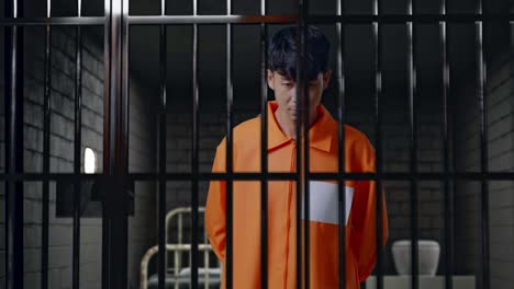 prisionero masculino asiático con esposas de pie en la cárcel, girándose para mirar a la cámara y sacudiendo la cabeza molesto por lo que hizo