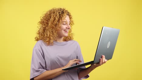 smiling woman with curly hair using laptop on yellow background