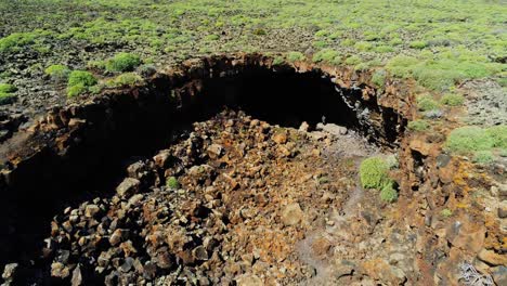 Dark-deep-cave-in-majestic-landscape-of-Lanzarote-island,-aerial-fly-away-reveal-landscape-view