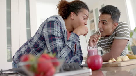 Happy-diverse-gay-male-couple-sharing-fruit-smoothie-drinking-with-straws-in-kitchen,-slow-motion