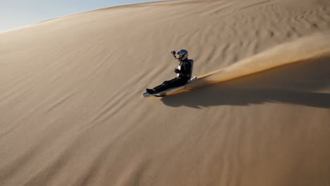 person sandboarding down a large sand dune