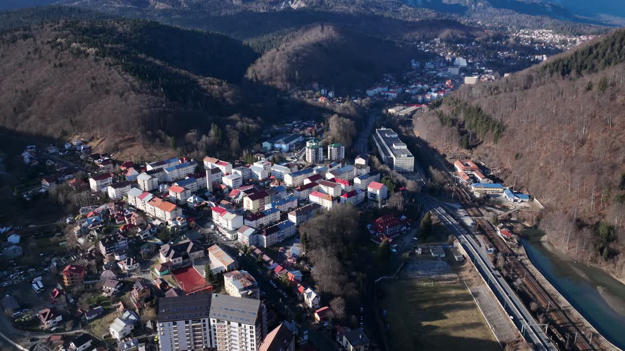 tiro aéreo inclinado hacia abajo sobre una pequeña zona residencial de sinaia a la luz del sol - carretera de montaña con coches de conducción
