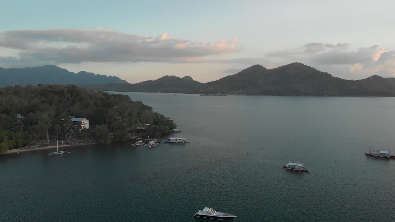Aerial pan drone shot flying over ocean, full of boats, panning around revealing resorts on Islands, in Philippine archipelago, at sunset, on a sunny warm evening, at Coron, Philippines, Asia
