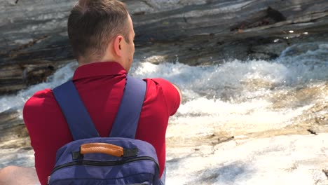 30s forest hiker travel man with backpack sitting and relax near mountain river. contemporary travel guy in nature scenic. healthy outdoor leisure time by the river