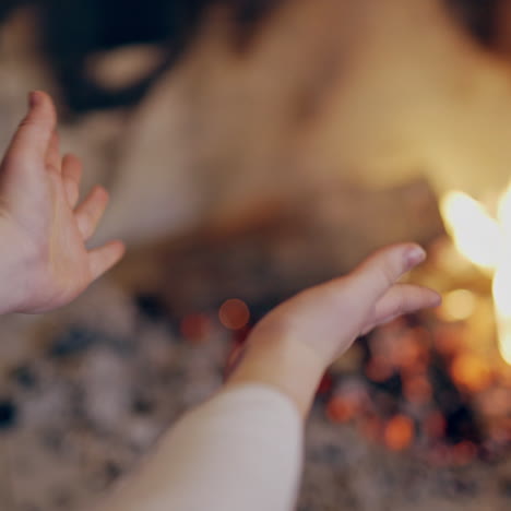 close-up footage of young woman warming cold hands at burning fireplace. woman rubbing hands in front of burning fireplace. girl is warming herself during winter in front of fire.
