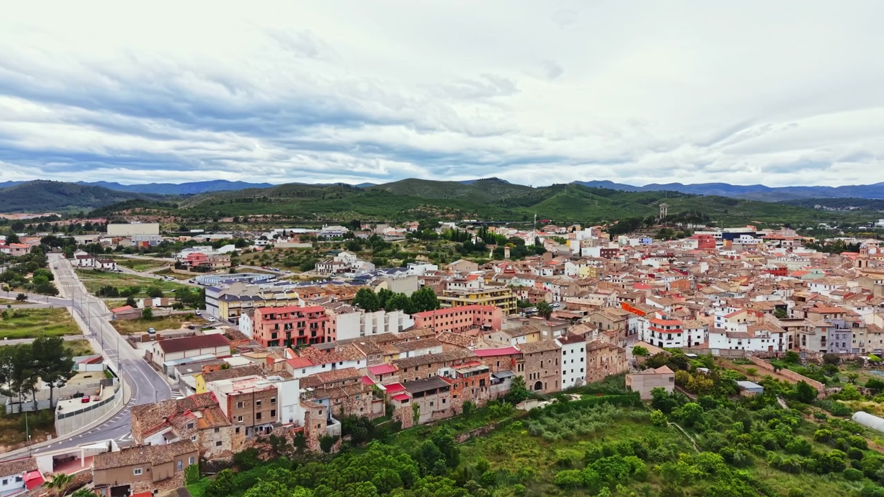 Vista de un pequeño pueblo rodeado de colinas con muchos edificios y carreteras, ubicado en una zona rural durante un día nublado.