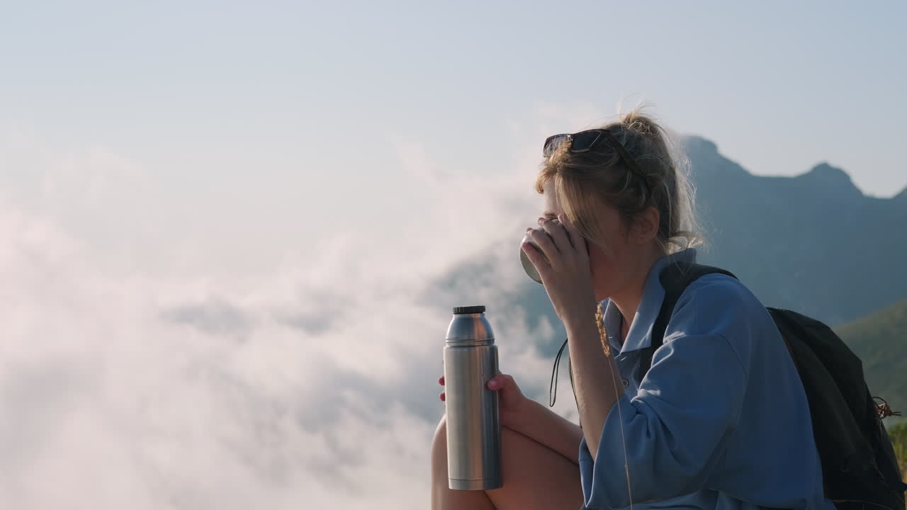 mujer disfrutando de una bebida en la cima de una montaña