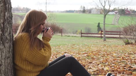 adult girl is drinking hot beverage at autumn scenery in slow motion filling relief by good taste