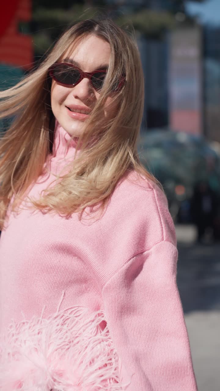 A woman in a pink sweater joyfully dances on a city street, surrounded by urban decor and vibrant colors, exuding happiness and energy on sunny day