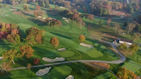 aerial in fall season, colorful leaves above golf course fairways during beautiful morning light