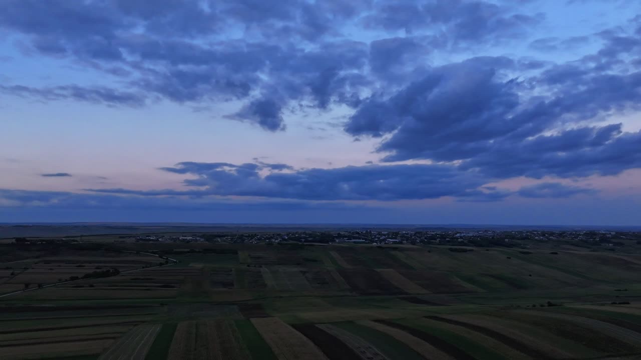 Hyperlapse aereo all'ora blu, sorvolo delle colline rumene, nuvole alla deriva sul paesaggio agricolo di Botoșani.