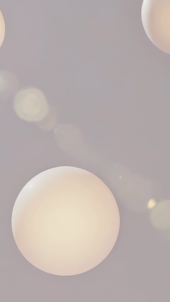 Video verticale: Inquadratura dinamica che mostra una grande sfera color crema illuminata che si sposta verso il centro, su uno sfondo grigio tenue.