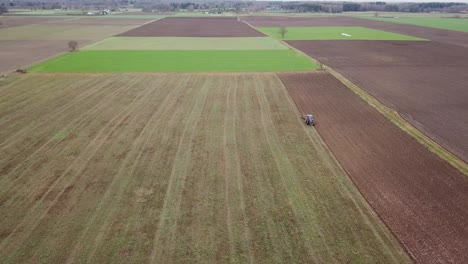 Wide-spinning-aerial-view-of-a-farm-with-various-types-of-crops-as-a-tractor-plows-the-fields