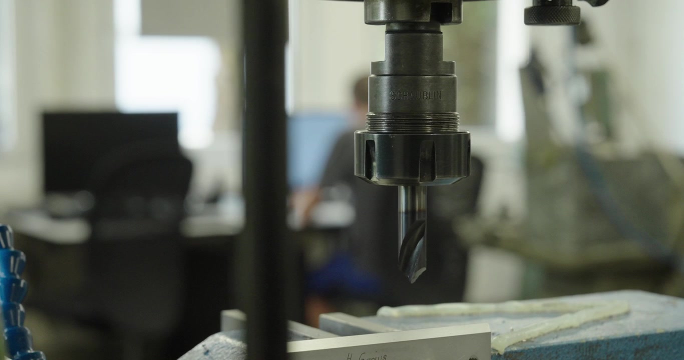 Gros plan d'une fraiseuse CNC au premier plan, tandis qu'un ingénieur travaille sur un ordinateur à l'arrière-plan, illustrant la fabrication de précision et la production industrielle