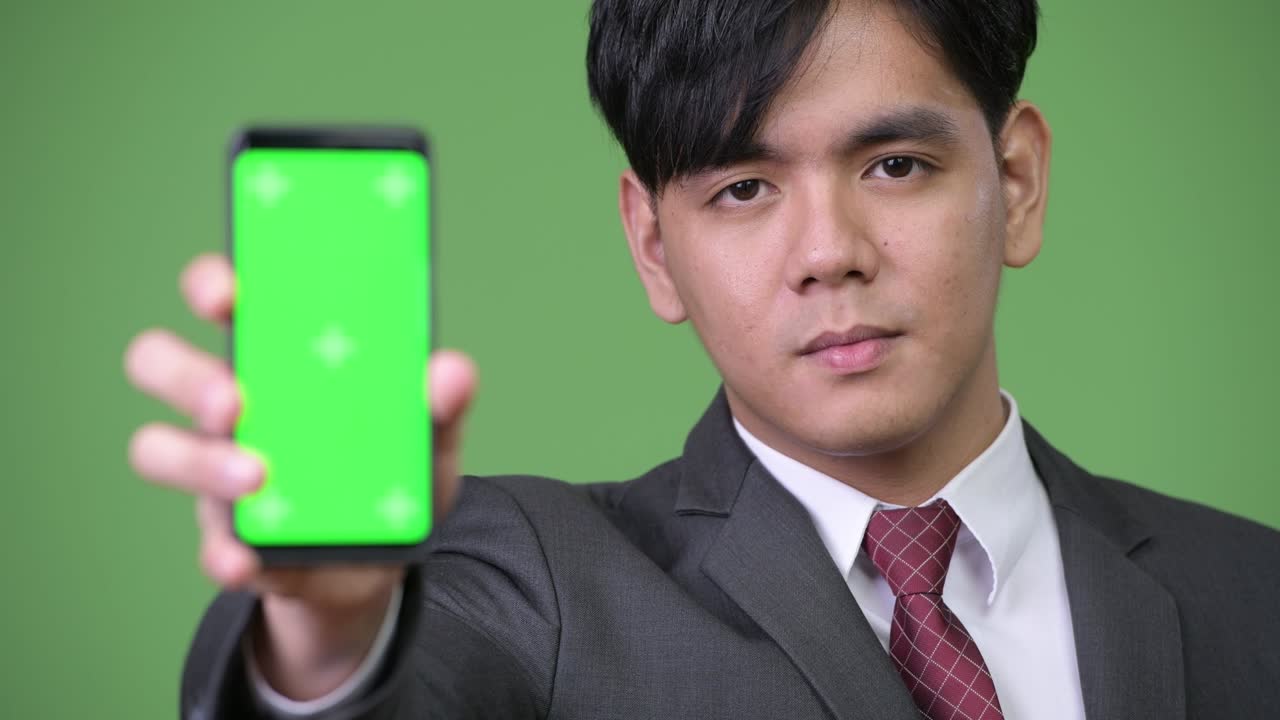 젊은 잘생긴 아시아 사업가 휴대전화를 보여줍니다.