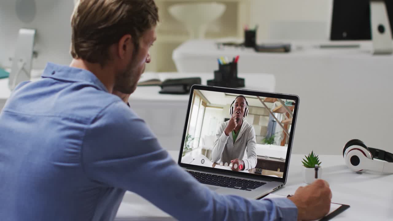 Caucasian male teacher taking notes while having a video call with african american boy on laptop