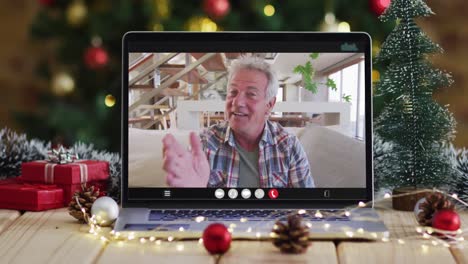 Hombre-Caucásico-Mayor-Saludando-En-Videollamada-En-Una-Computadora-Portátil,-Con-Adornos-Navideños-Y-árbol