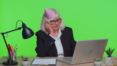 Sad-upset-lonely-senior-businesswoman-celebrating-birthday-party-alone,-holds-cake-at-green-office