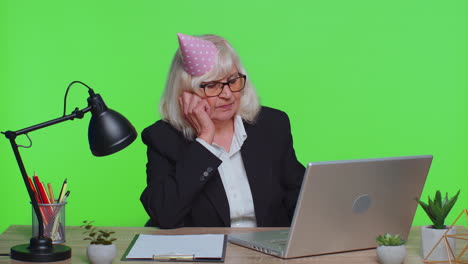 sad upset lonely senior businesswoman celebrating birthday party alone, holds cake at green office