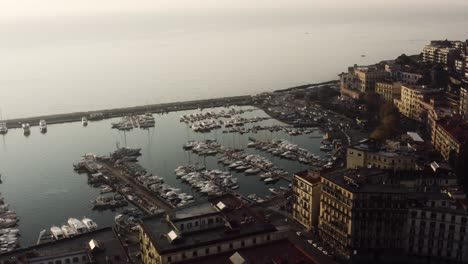 Aerial-tilt-down-shot-showing-marina-port-of-Naples-City-during-golden-sunset-and-sea-in-background,-Italy