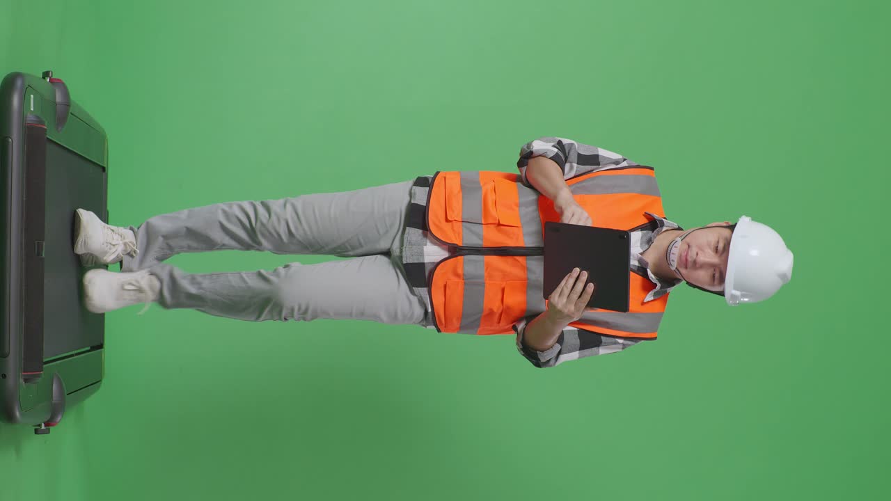 녹색 화면 배경 스튜디오에서 는 동안 태블릿을 사용하여 안전 헬을 착용 한 아시아 남성 엔지니어의 전체 몸