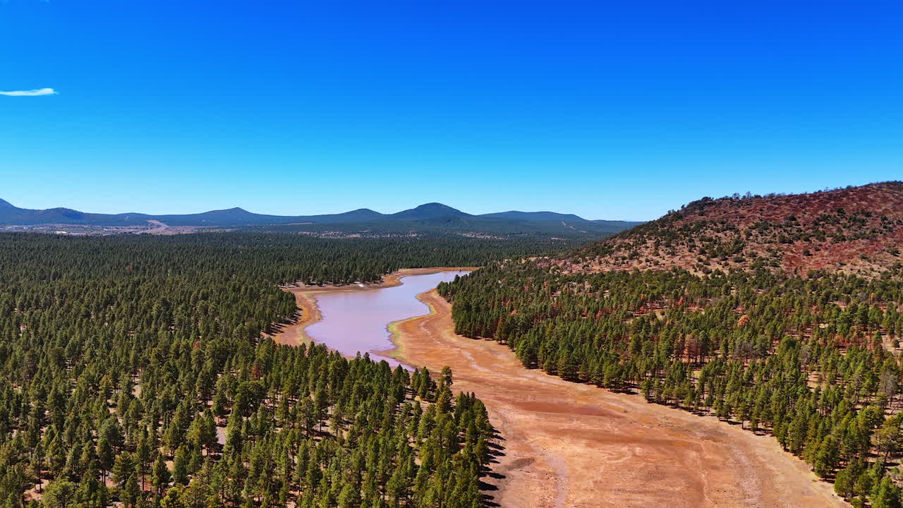 Approaching a shallow river dried out in the sun. Footage over the nature landscapes of Arizona with pine tree woods and mountains at backdrop