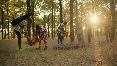 A-group-of-people-in-hiking-clothes-stop-for-a-break-and-arrange-their-things.-Stopping-and-resting-during-the-hike,-preparing-an-overnight-shelter-in-the-summer-forest.-A-group-of-people-in-plaid-shirts-stop-for-a-break