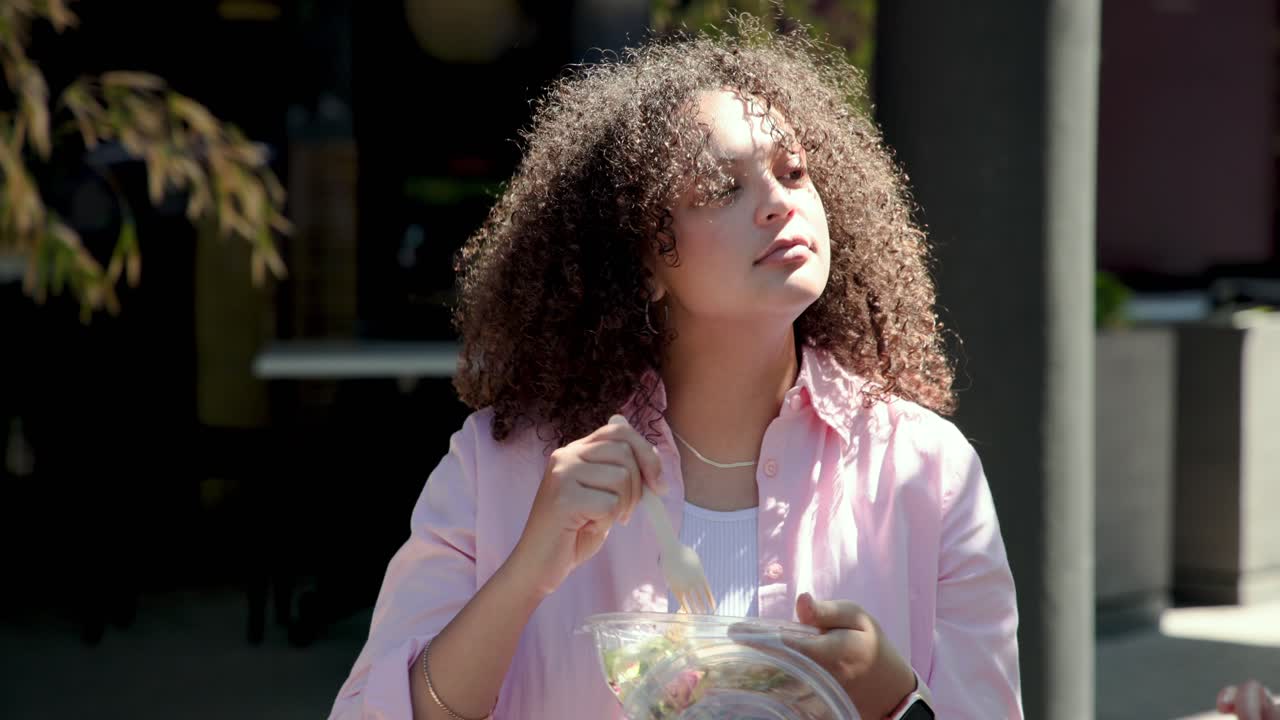 Verandada şeffaf kabı açan, plastik çatalla yemeğini karıştıran ve tadan yetişkin Afro-Amerikalı kadın.