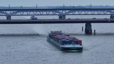 Aerial-of-Large-cargo-ship-carrying-shipping-containers-passing-under-a-busy-bridge-with-cars-driving-by