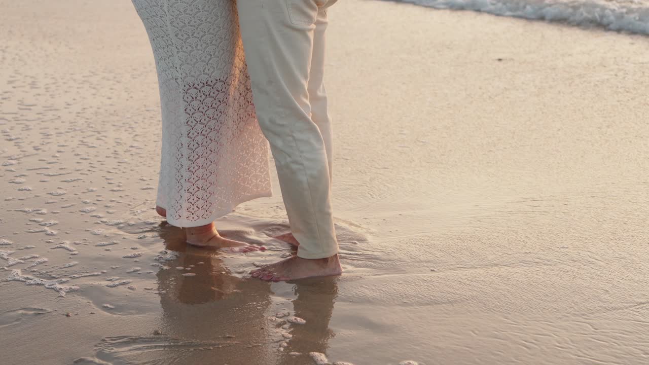 bare feet of couple touching seafoam in soft light on beach shore