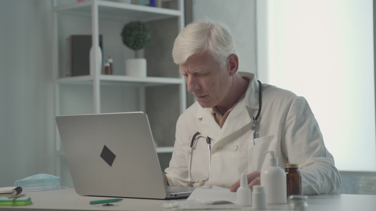 A Grey Haired, Middle Aged Doctor Consults On His Laptop The Composition Of A Medicine 1