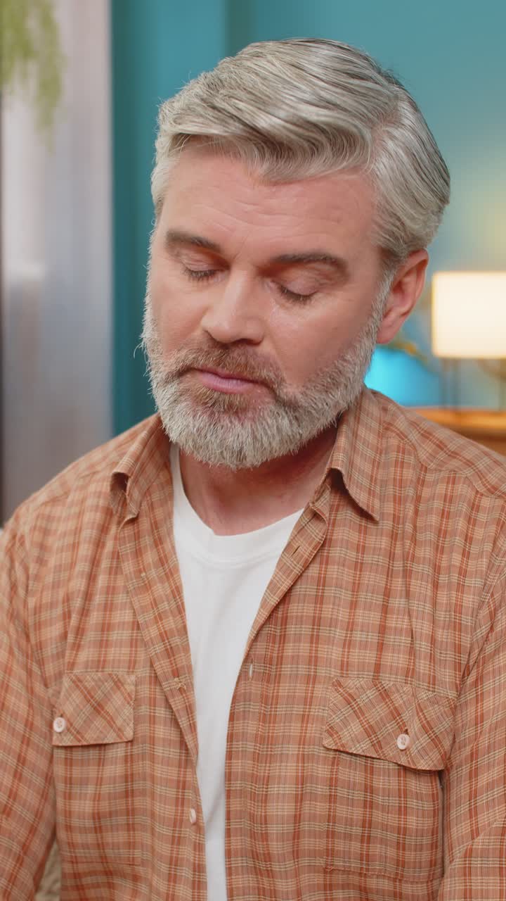 Mature man sitting on sofa holding smartphone expressing stress after receiving bad news at home
