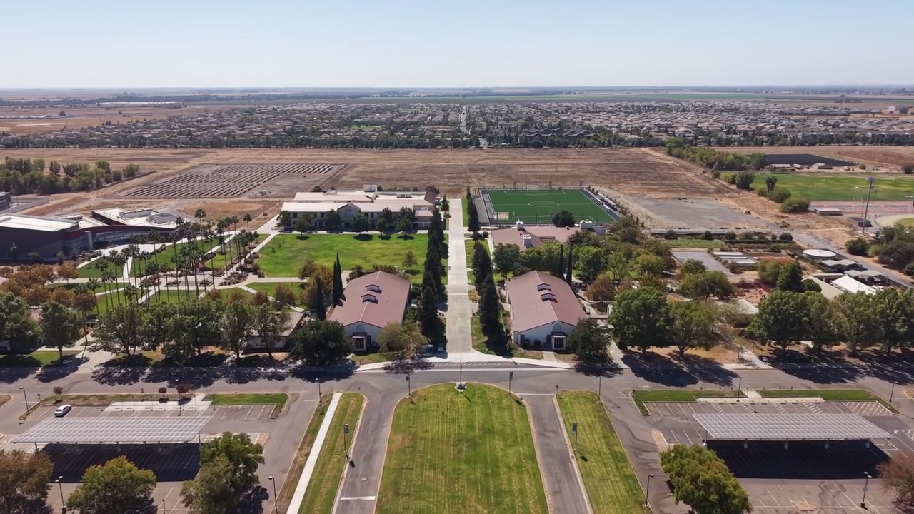 Drone push in shot of the Woodland Community College campus, its buildings, parking lots, and the surrounding residential area under a clear blue sky in sunny California