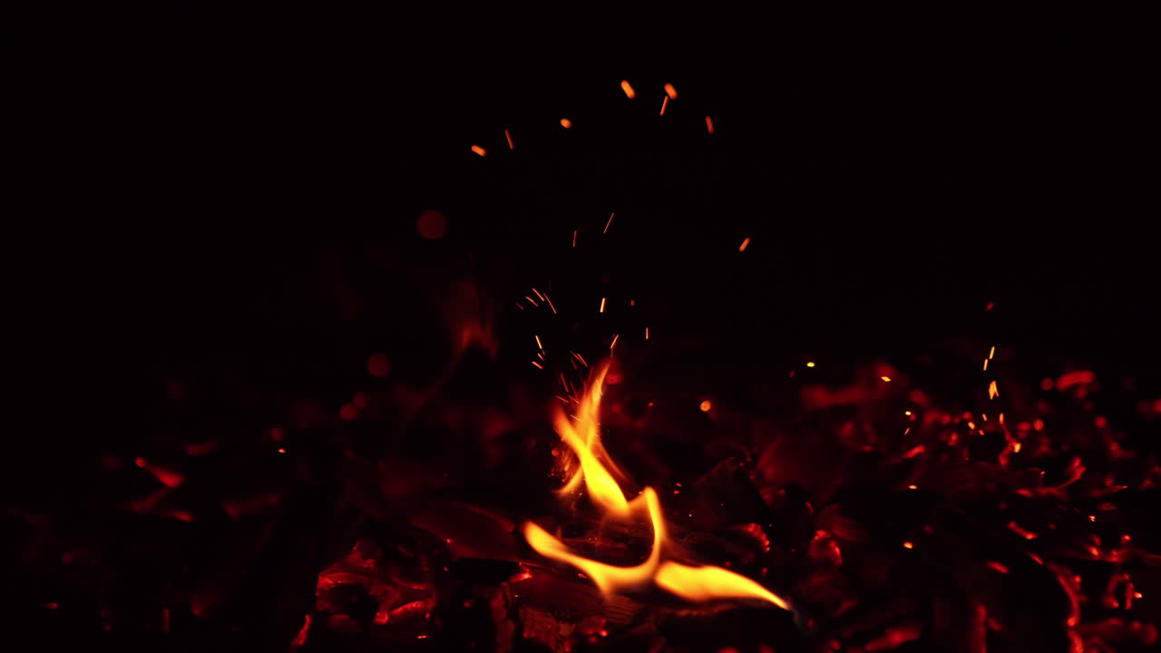 Embers of bonfire are burning out. Close up. Hitting beautiful charcoals smoldering in campfire and tiny sparks go up.