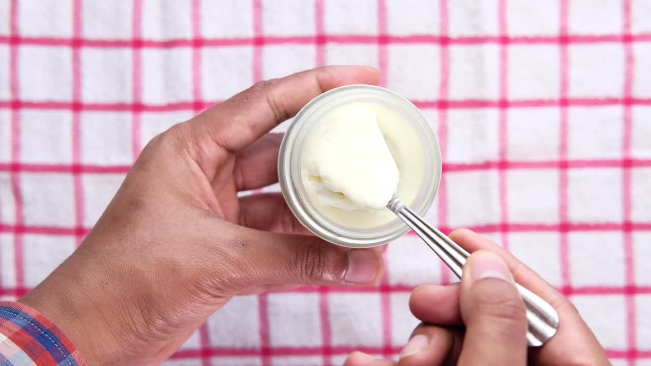 Persona che mangia yogurt da un piccolo vasetto con un cucchiaio