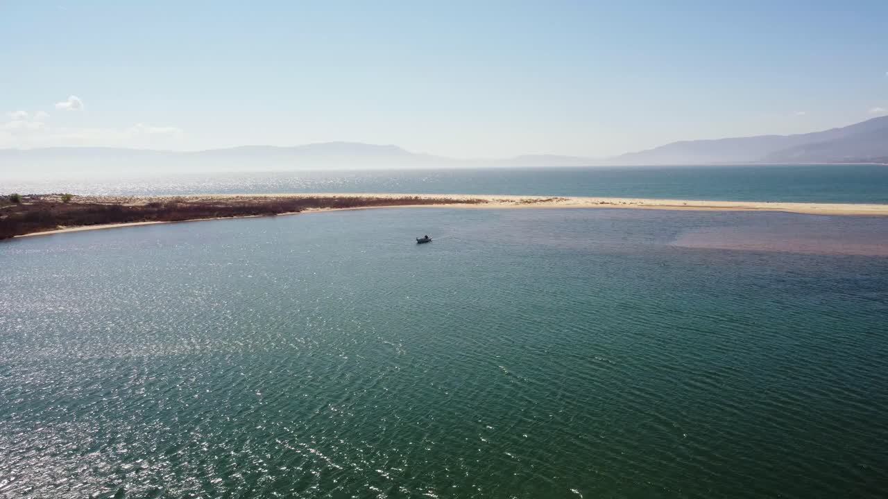 Aerial pull back with small fishing boat on a lagoon next to the ocean