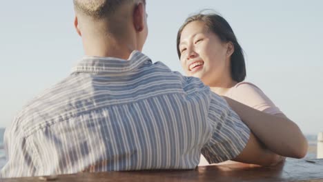 happy biracial couple embracing on promenade by beach, in slow motion