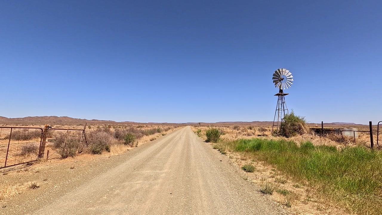 Einsame Windmühle dreht sich langsam an einer abgelegenen Wüsten-Schotterstraße.